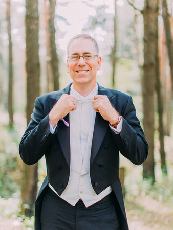 Half-length portrait of the cheerful groom corrects his white bow-tie. Forest location.の写真素材