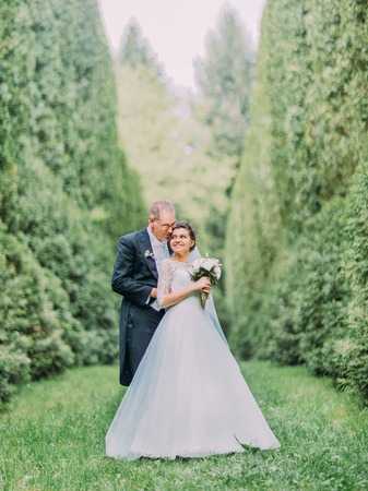 Romantic photo of the cheerful newlyweds hugging in the blooming garnde of high bushes.の写真素材