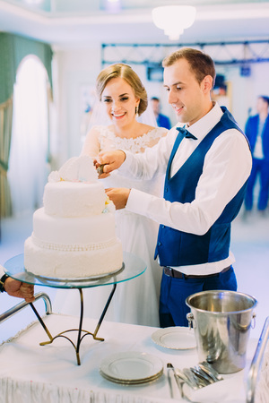 Vertical photo of the happy newlyweds cutting the first piece of the wedding cake.の写真素材