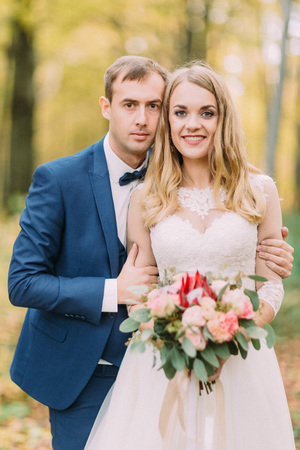 Half-length portrait of the groom hugging the bride with the wedding bouquet back. Autumn composition.の写真素材