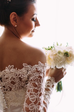 The back view of the bride in lace dress holding the wedding bouquet of white roses.の写真素材