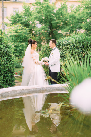 Happy newlyweds holding hands near the fountain in the garden.の写真素材