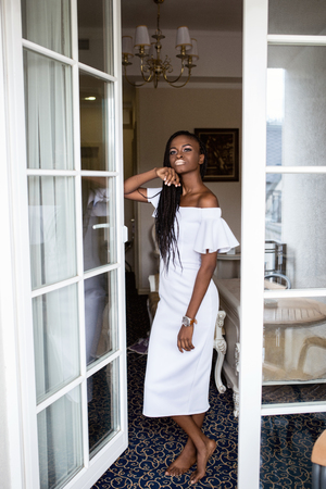 Attractive afro american woman standing in the room near the french window in beautiful long white dress.の写真素材