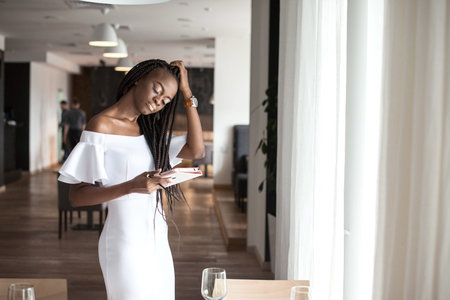 Beautiful african american girl standing near the table in a restaurant with the tablet in her hands.の写真素材