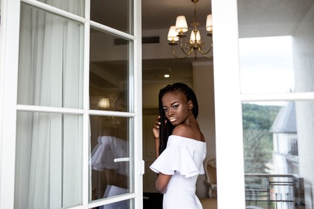 African american girl posing by open window or door wearing white dress.の写真素材