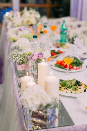 The wedding table set covered with different dishes and candlesの写真素材