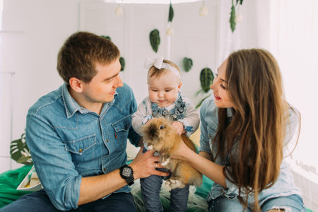 Cheerful family is playing with the little baby. The baby is petting the rabbit.の写真素材