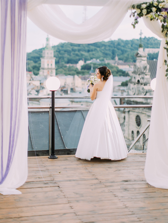 The full-length back view of the bride with the wedding bouquet standing near the balcony fence.の写真素材