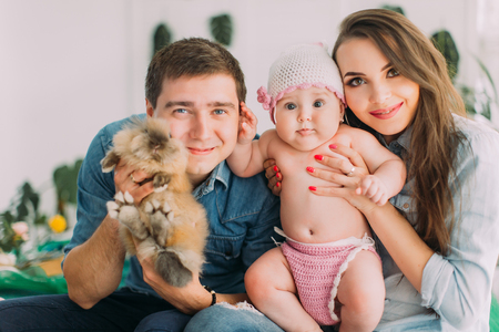 Close-up portrait of the family. The smiling mother is holding newborn while the father is holding the lovely rabbit.の写真素材