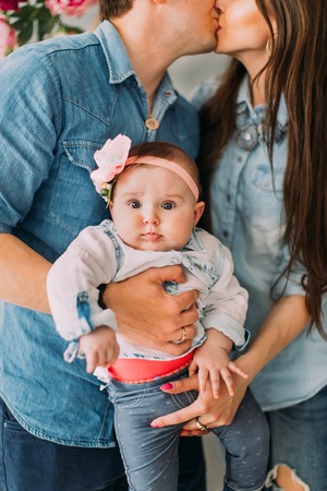 The close-up portrait of the baby at the background of the kissing parents holding the child.の写真素材