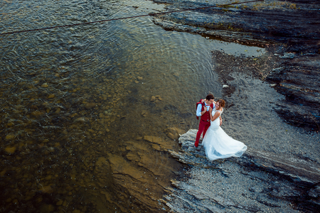 Romantic above portrait of the smiling newlyweds tenderly hugging at the river bank during the sunny day.の写真素材