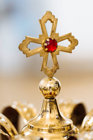 Golden wedding crowns with precious stones lying on the table in the church. golden cross with red...