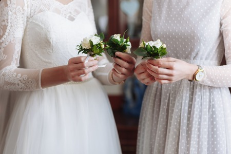Beautiful wedding boutonier with white and green flowers in the hands of the bride and girlfriends in white dresess. morning of the brideの写真素材