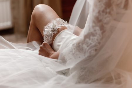 Woman wearing a garter on the leg. The bride holds in hand lose-up garter in hotel room. morning preparation wedding concept.の写真素材