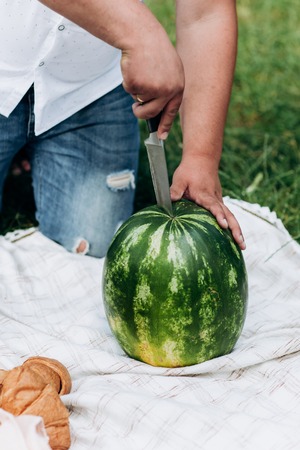 Man cuts a watermelon in two half onoutdoors. Hands close upの写真素材