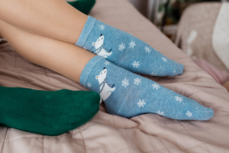 Legs with cute blue socks with white bears and green socks on the bedの写真素材