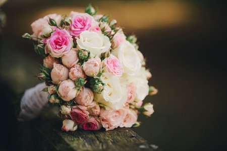 Stylish wedding bouquet bride of pink roses, white carnation and green flowers and greens with ribbons lying. Close up. Side view. Wedding decor. Artwork. beautiful wedding bouquet