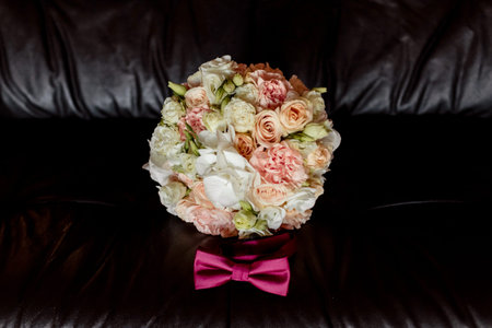 wedding butterfly tie and Bouquet of bridewith pink and white roses lying on the couch on a dark background. front viewの写真素材