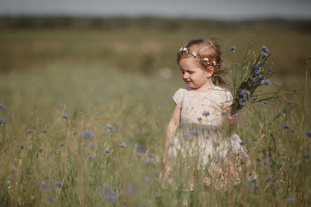 young little girl with long hair, white dress lonely walking in the poppy field and collecting flowers for a bouquet. little girl with a bouquet of wild flowersの写真素材
