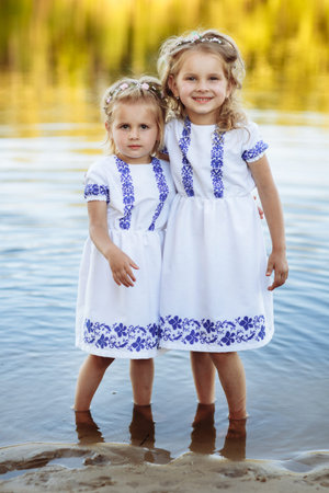 Two adorable little sisters laughing and hugging on warm and sunny summer day. two sisters in white dresses near the waterの写真素材