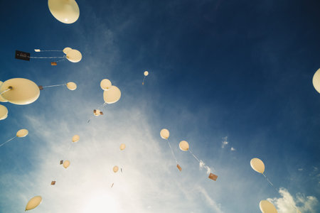 White balloons fly up into the blue sky. The release of festive balloons in the clouds. Celebration...