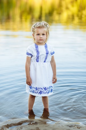 portrait of a little girl who stands in water in a white dress. beach in summerの写真素材