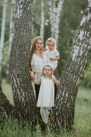 family photo mom with daughters in the park. Photo of young mother with two cute kids outdoors in spring time, beautiful woman with daughter having funの写真素材