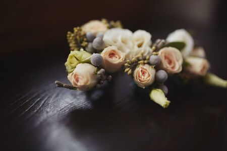 The bride holding in hand close-up the groom's buttonhole flowers with white roses, and green and greenery. Bride's Preparations. Wedding Morning concept.の写真素材