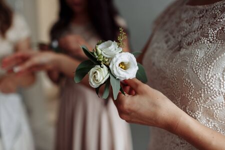 The bride holding in hand close-up the groom's buttonhole flowers with white roses, and green and greenery. Bride's Preparations. Wedding Morning concept.の写真素材