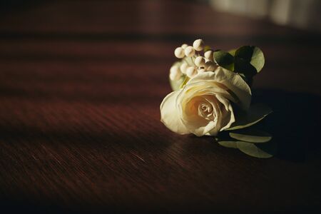 The bride holding in hand close-up the groom's buttonhole flowers with white roses, and green and greenery. Bride's Preparations. Wedding Morning concept.の写真素材
