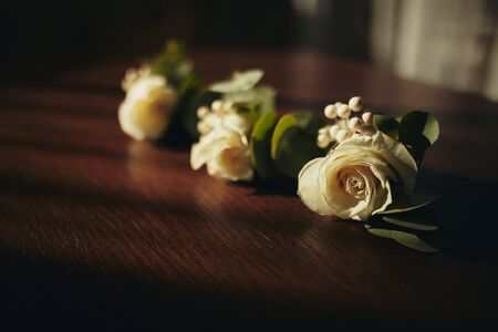 The bride holding in hand close-up the groom's buttonhole flowers with white roses, and green and greenery. Bride's Preparations. Wedding Morning concept.の写真素材