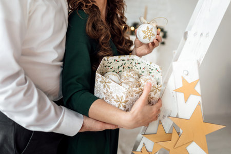 Decorating Christmas tree. Wife and husband holding a box with christmas toys in scandinavian style....
