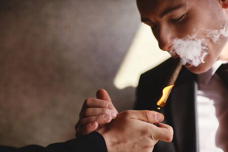 elegant man wearing suit and white shirt smoking cigar indoor shot, closeup, cigar smoke, selective focusの写真素材