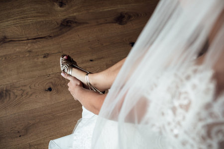 Elegant Female puts hands on wedding shoes on a background white dress, Wedding morning preparation in homeの写真素材