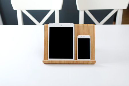 office workplace. a white tablet and a smartphone with a black screen on a stand on a white table