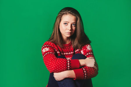 Young woman in Christmas sweater on green background.
