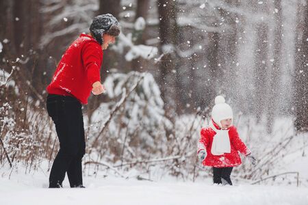 Portrait of happy little girl in red coat with dad having fun with snow in winter forest. girl playing with dadの写真素材