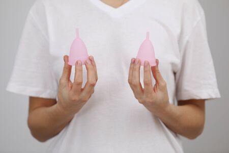 Pink menstrual cups. Close up of woman hand holding different size menstrual cups. Women health concept, zero waste alternativesの写真素材