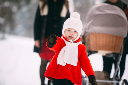 portrait of pretty little girl in red coat enjoying winter day. In the background, her family, mom,...