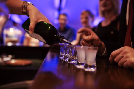 Bartender pouring strong alcoholic drink into small glasses on bar, shots in a nightclub or bar.の写真素材