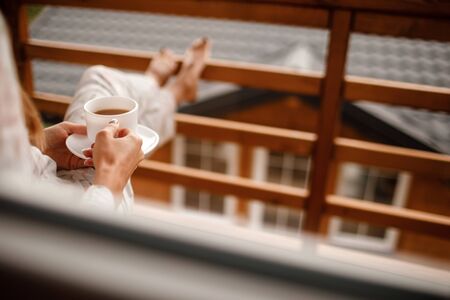 young woman in stylish nightwear enjoy drinking coffee or tea outdoor on balcony in the morning and looks at the mountainsの写真素材