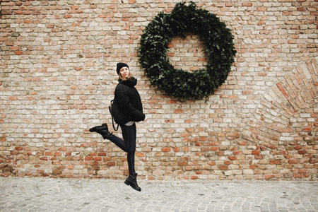 stylish tourist girl with backpack jumps near the wall. On the wall of the old brick a large...