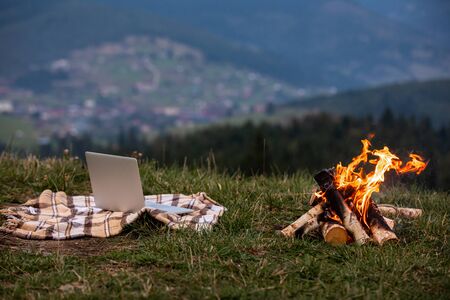 laptop laptop on plaid near campfire. behind mountain backgroundの写真素材