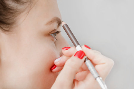 Beautiful girl paint eyebrows brown. Girl doing makeup in front of a mirror. The girl was caring for...