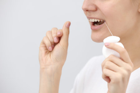Oral hygiene and health care. Smiling women use dental floss of white healthy teeth on a white...