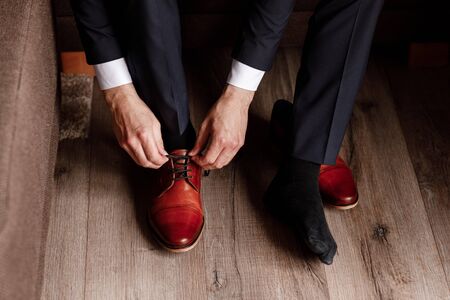 groom tied the laces on the shoes close up. business man is hanging shoes indoor in hotel room. mans hands and pair of leather mens shoes. meeting of the bridegroom. business mans morning.の写真素材