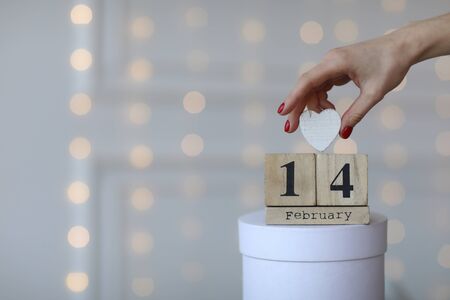 Valentine's day concept. Date 14 February on wooden cube calendar on a white gift box and white heart in hand. Bokeh golden and white backgroundの写真素材