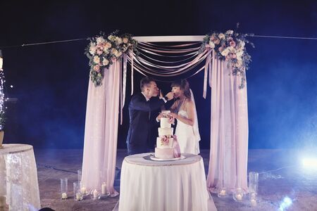 gorgeous bride and stylish groom tasting their stylish wedding cake. happy newlywed couple eating piece of cake, funny emotional momentの写真素材