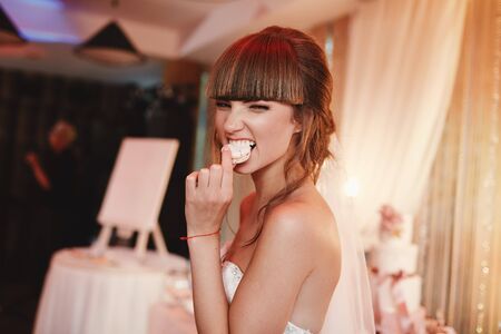 portrait of stylish cheerful bride eating french macaroon dessert. wedding and holiday concept.の写真素材