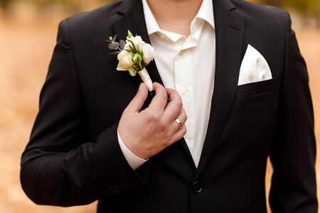 white roses flowers in buttonhole, the groom is dressed in a dark suit and a white shirt. Wedding ceremony, elegant suit. Outfit of the dayの写真素材